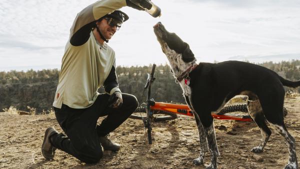 A mountain biker shares a drink of water with a dog