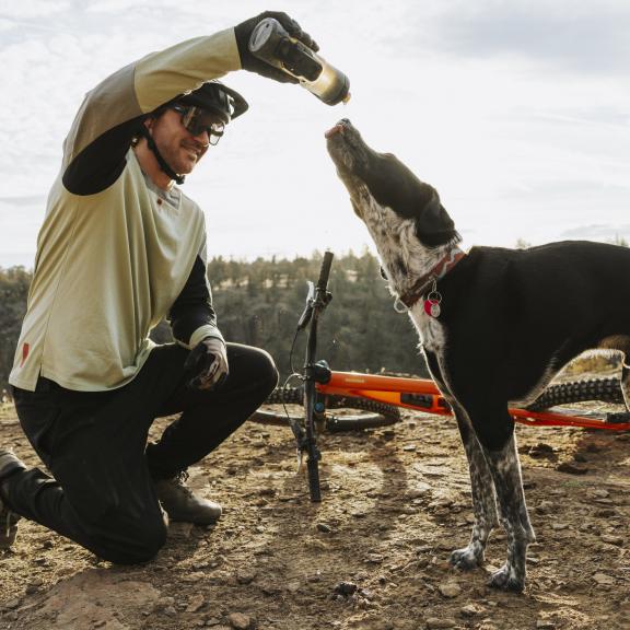 A mountain biker shares a drink of water with a dog