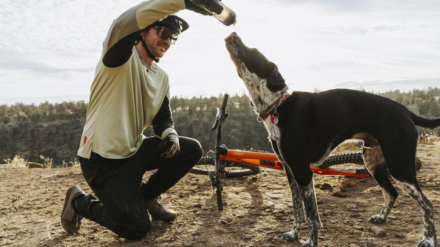A mountain biker shares a drink of water with a dog